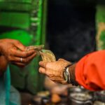 A close-up shot of two people exchanging currency in an outdoor market setting.