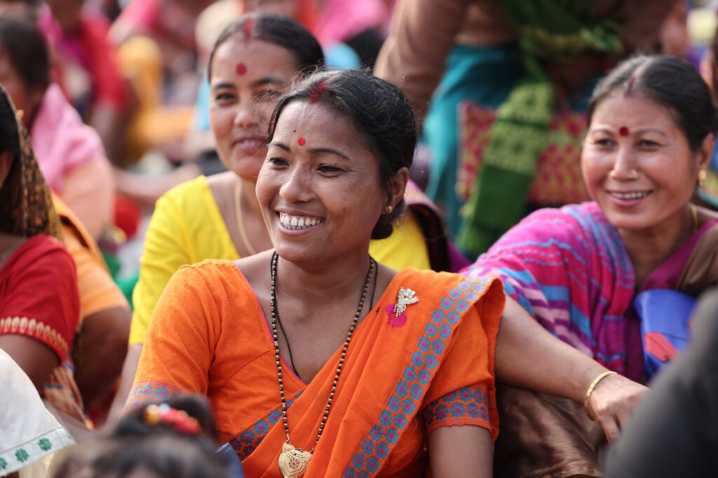 Smiling Indian women in colorful traditional clothing engaging in a lively outdoor gathering.