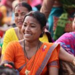 Smiling Indian women in colorful traditional clothing engaging in a lively outdoor gathering.