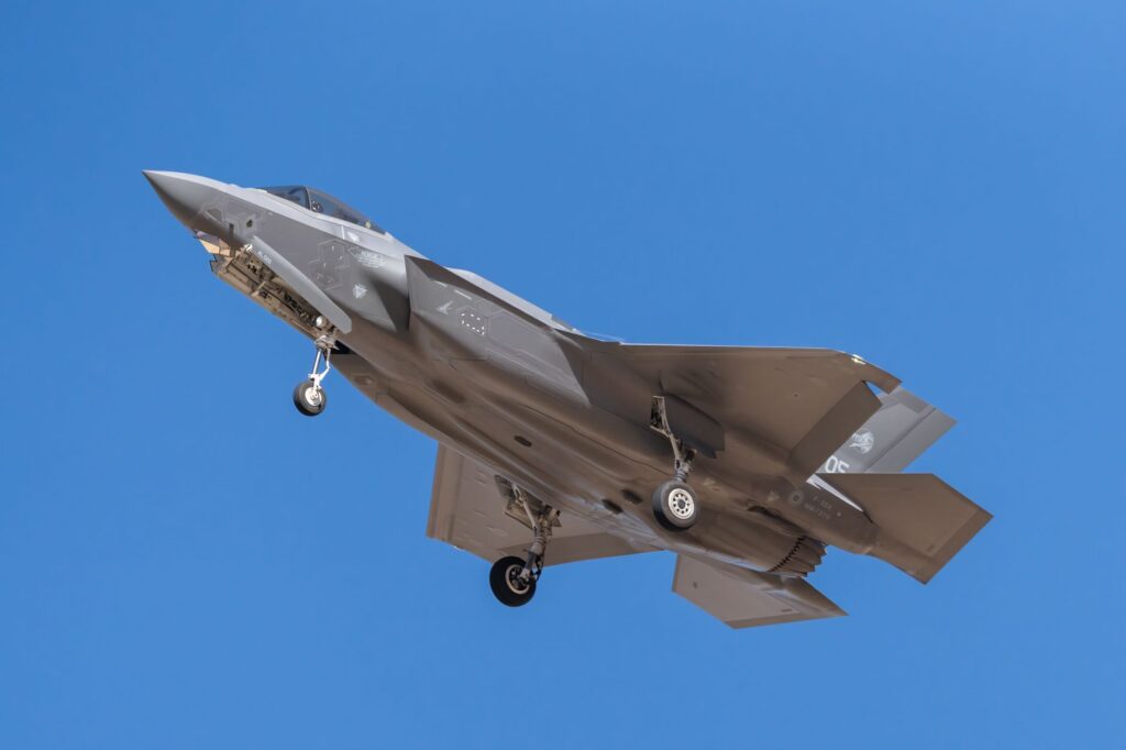 F35 fighter jet in flight with landing gear visible against clear blue sky, showcasing military aviation prowess.