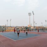 Players engaged in a volleyball match on an outdoor court in a cityscape.