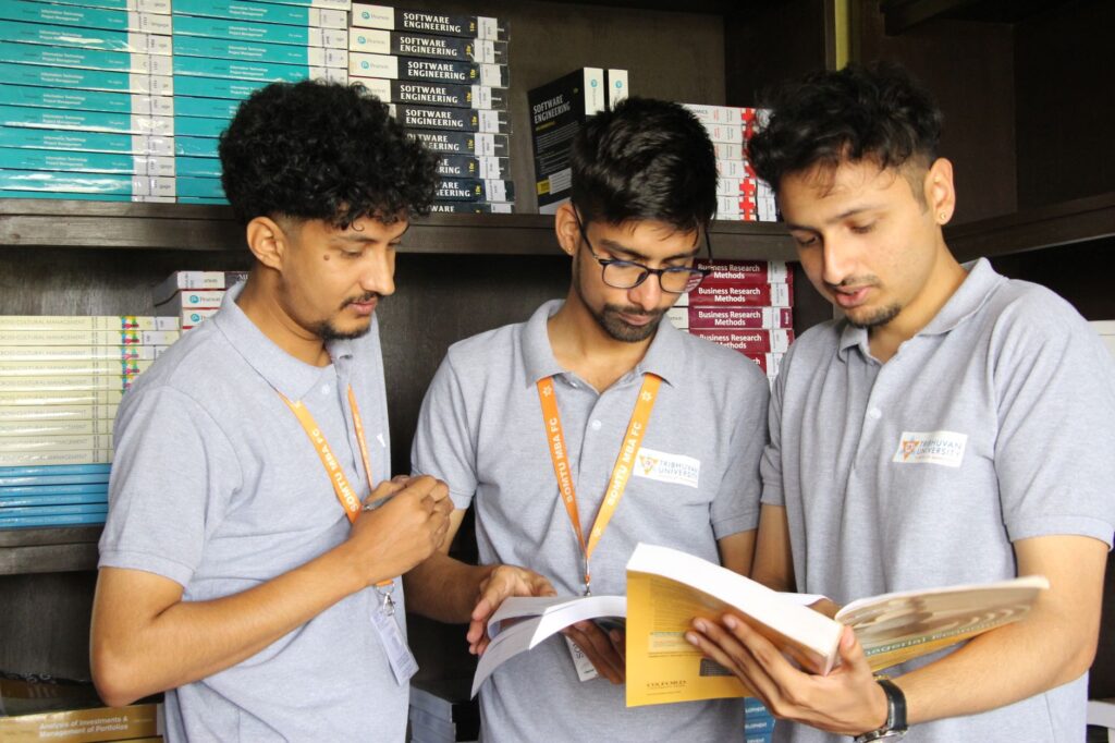 Three male students studying in a library, focused on business books, at Nepal university.