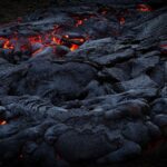 Close-up of glowing lava flowing over dark volcanic rock, showcasing intense heat and dramatic landscapes.