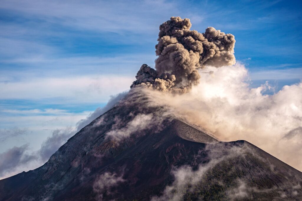 A breathtaking view of an erupting volcano with large plumes of smoke against a clear sky.