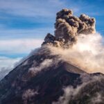 A breathtaking view of an erupting volcano with large plumes of smoke against a clear sky.
