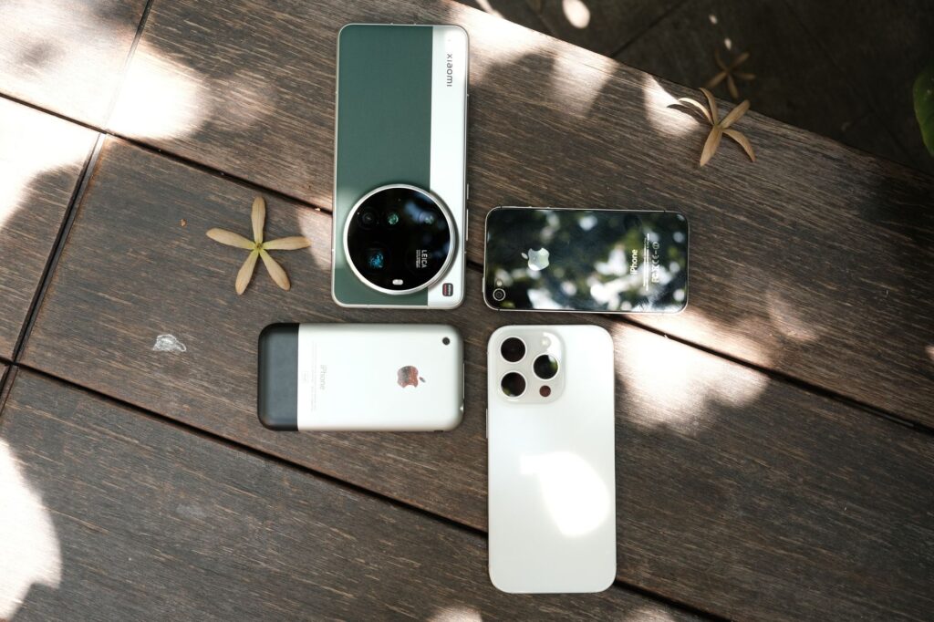 Assorted smartphones displayed outdoors on a wooden table under dappled sunlight.