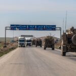 US military convoy travels on a highway in Al Hasakah, Syria, under blue skies.