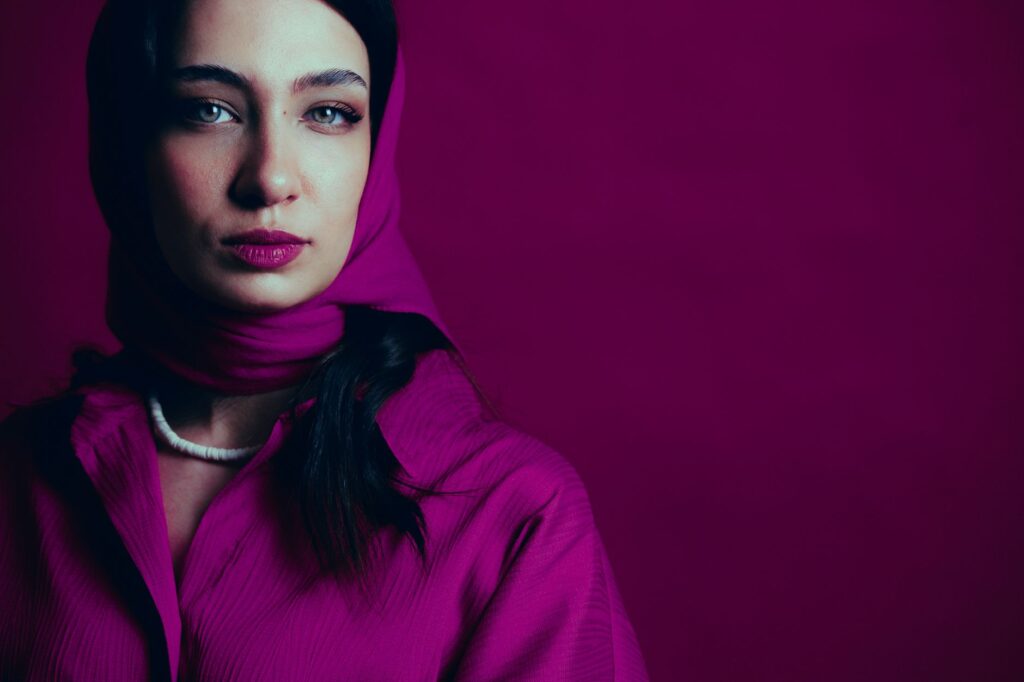 Close-up portrait of a woman wearing a magenta hijab against a matching background.