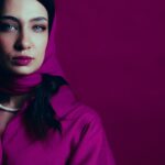 Close-up portrait of a woman wearing a magenta hijab against a matching background.