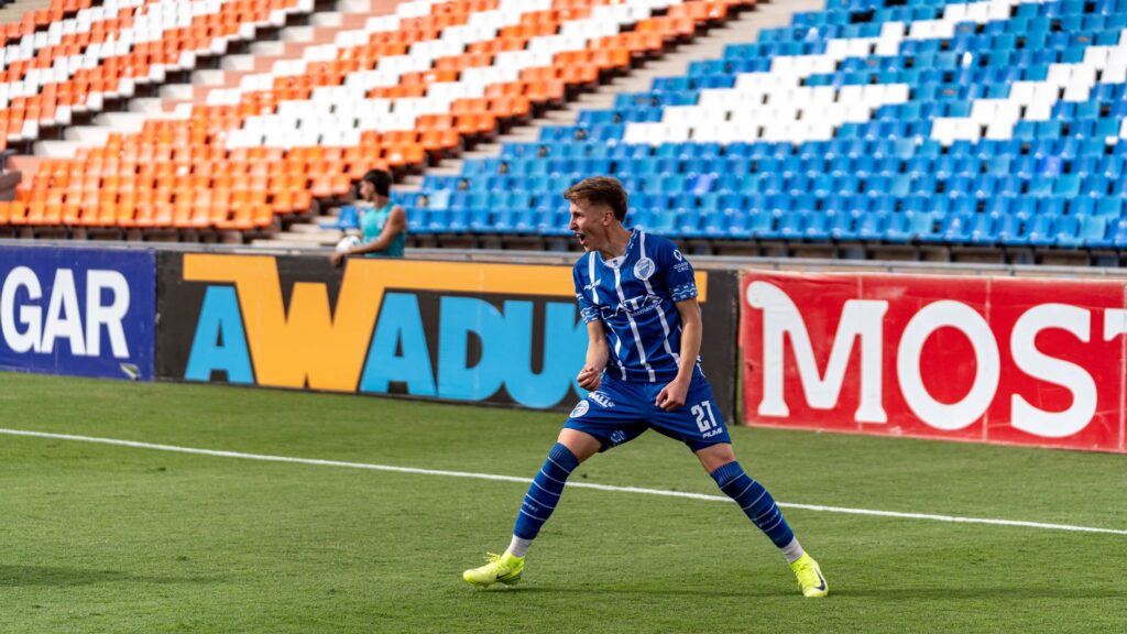 Soccer player in blue uniform celebrates goal on a sunny field