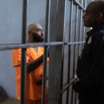 A guard converses with an inmate inside a prison cell, highlighting the justice system setting.
