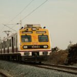 A suburban train traveling on tracks next to a derailed train on a cloudy day.