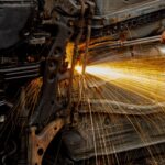 Mechanic welding car engine parts, with bright sparks flying. Hands-on automotive repair scene in workshop.