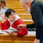 A professor assisting a college student during class in a university lecture hall.