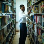 Young male student explores bookshelves in university library for research.