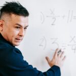 A mathematics instructor explaining algebraic equations on a whiteboard in a classroom setting.