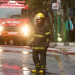 Firefighter in uniform stands near a fire truck in the street during an emergency operation.