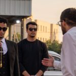 Casual conversation among fashionable men wearing sunglasses outdoors at sunset.