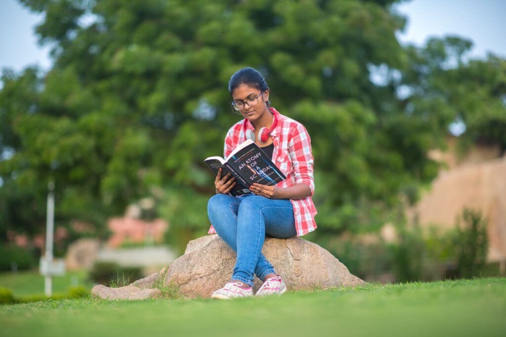 Young woman in Hyderabad engrossed in reading a book, sitting on a rock in a park.