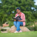 Young woman in Hyderabad engrossed in reading a book, sitting on a rock in a park.