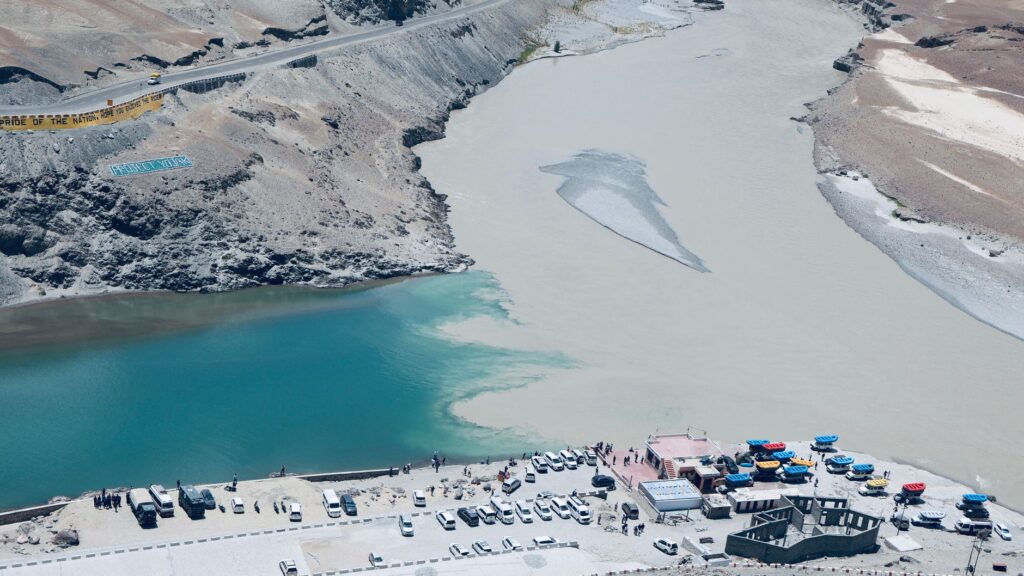 Aerial shot of two rivers meeting in a mountainous region with vehicles and visitors nearby.