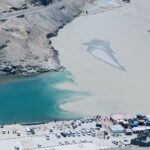 Aerial shot of two rivers meeting in a mountainous region with vehicles and visitors nearby.