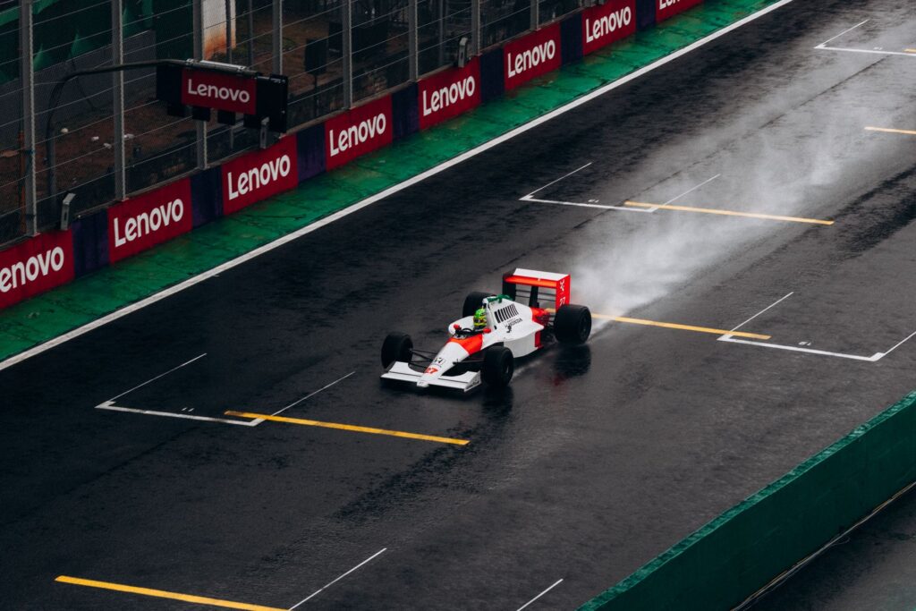 A classic Formula 1 car races on a wet track at Interlagos, Brazil, leaving a trail of spray behind.