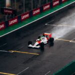 A classic Formula 1 car races on a wet track at Interlagos, Brazil, leaving a trail of spray behind.