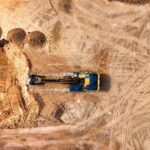 Aerial photo of an excavator working on a large empty construction site.