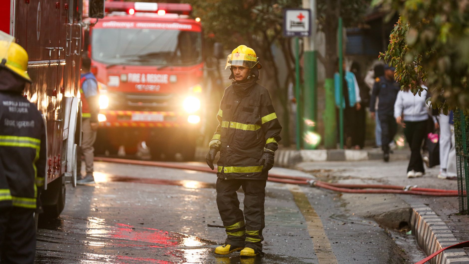 Firefighter in uniform stands near a fire truck in the street during an emergency operation.