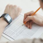 Close-up of a student writing answers on a test sheet with a pencil and smartwatch.