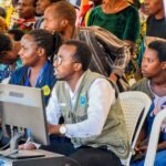 A diverse group of adults engaging with technology at a community event in Rwanda.