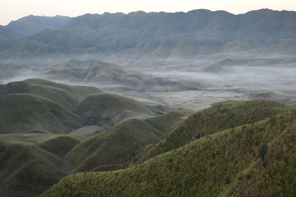 Breathtaking view of fog-laden rolling hills and valleys in Dzukou Valley, showcasing nature's tranquility.