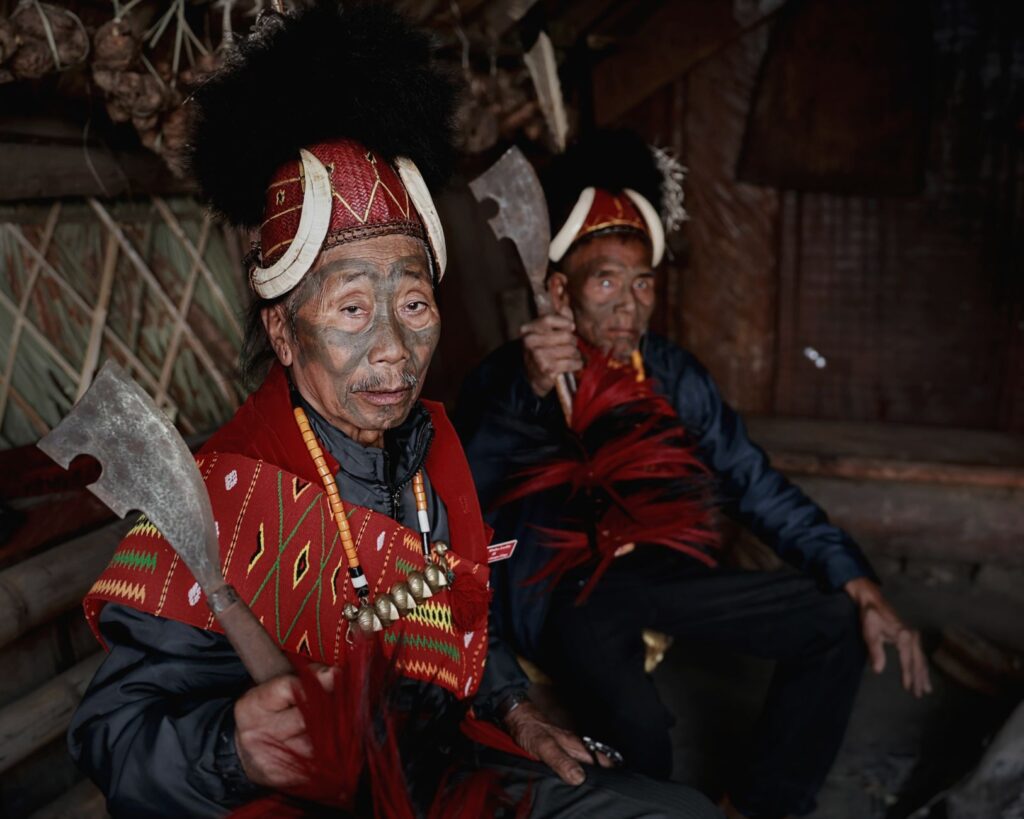 Portrait of Naga tribal warriors in traditional attire inside a rustic hut.