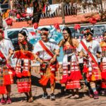 A group of people performing a traditional cultural dance outdoors, wearing tribal costumes.