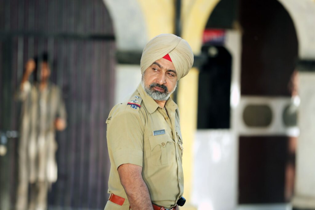 Sikh police officer in uniform standing outdoors with focused expression.