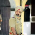 Sikh police officer in uniform standing outdoors with focused expression.