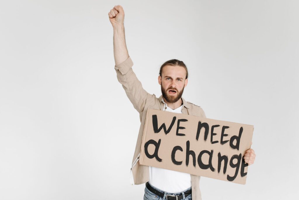 Man raising fist with protest sign demanding change in studio setting.