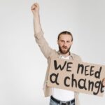 Man raising fist with protest sign demanding change in studio setting.