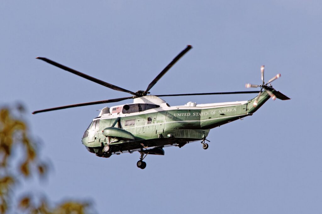 A SH-3 Sea King helicopter with USA markings flying outdoors on a clear day.
