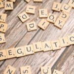 Wooden letter tiles spelling 'Regulation' on a textured wood background, conveying themes of compliance and structure.