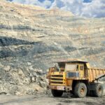 A large yellow mining truck in a rocky quarry under a clear sky.