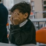 A child with hands covering face, experiencing bullying in a school setting.