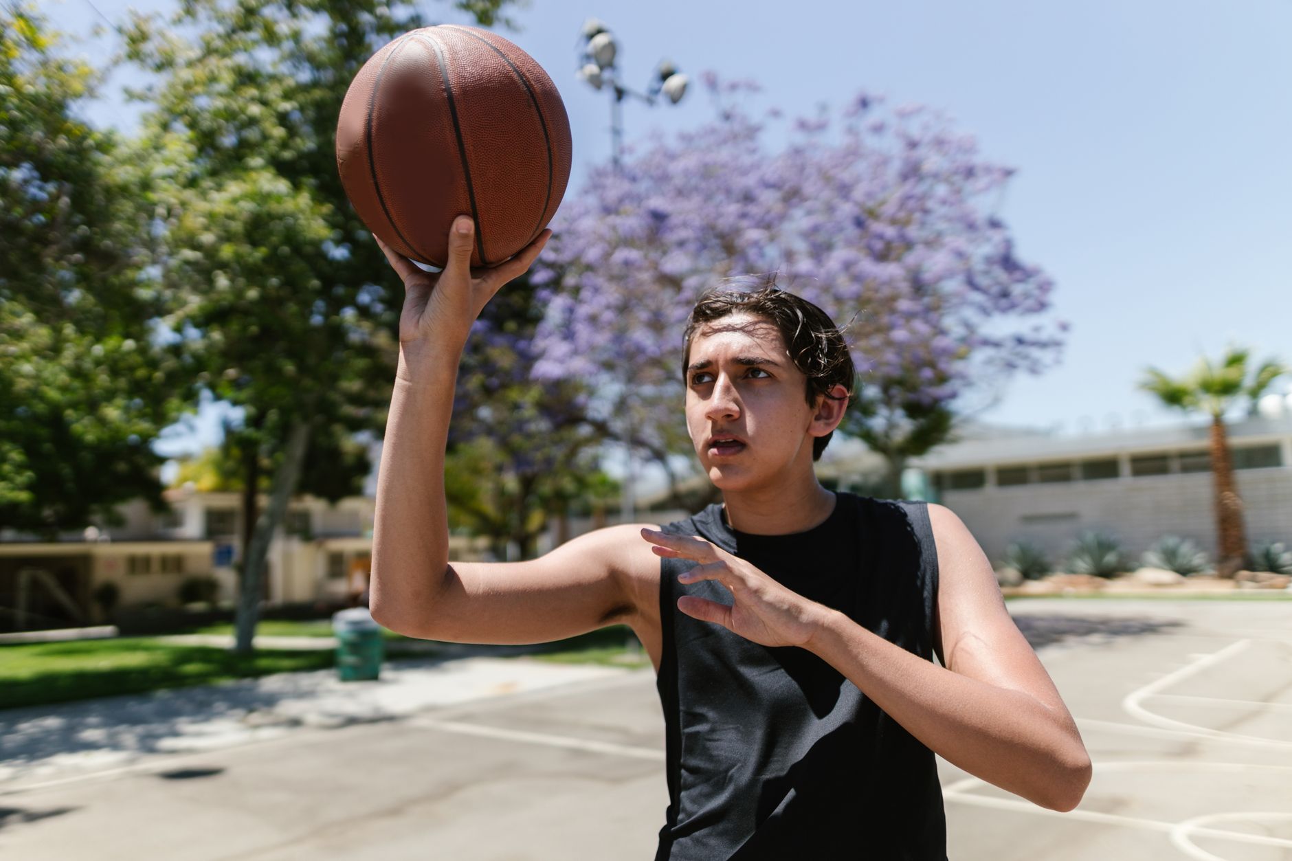 Young male teenager playing basketball on an outdoor court, aiming for a shot.