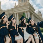 Group of graduates in caps and gowns celebrating outside a grand building.