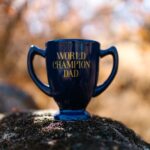 Blue cup with 'World Champion Dad' text placed on a rock with blurred nature background.