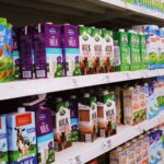 Various colorful boxes of milk placed on shelves with prices in modern supermarket