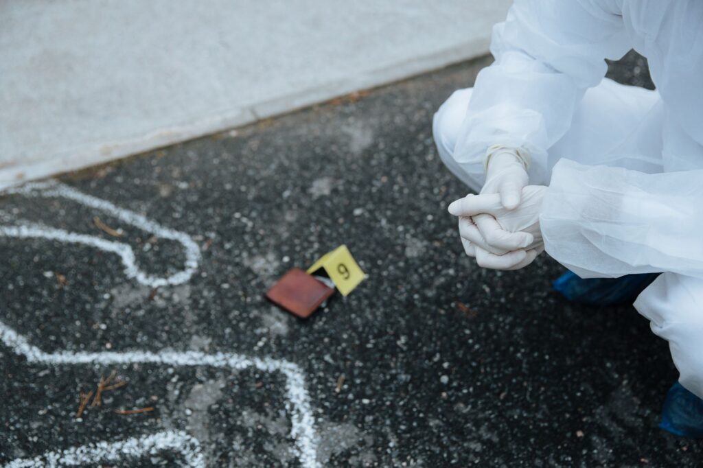 Forensic investigator examines crime scene outline on asphalt in protective suit.