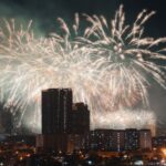Dazzling fireworks light up the evening sky above an urban skyline, creating a festive atmosphere.