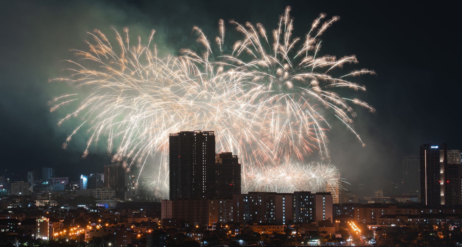 Dazzling fireworks light up the evening sky above an urban skyline, creating a festive atmosphere.